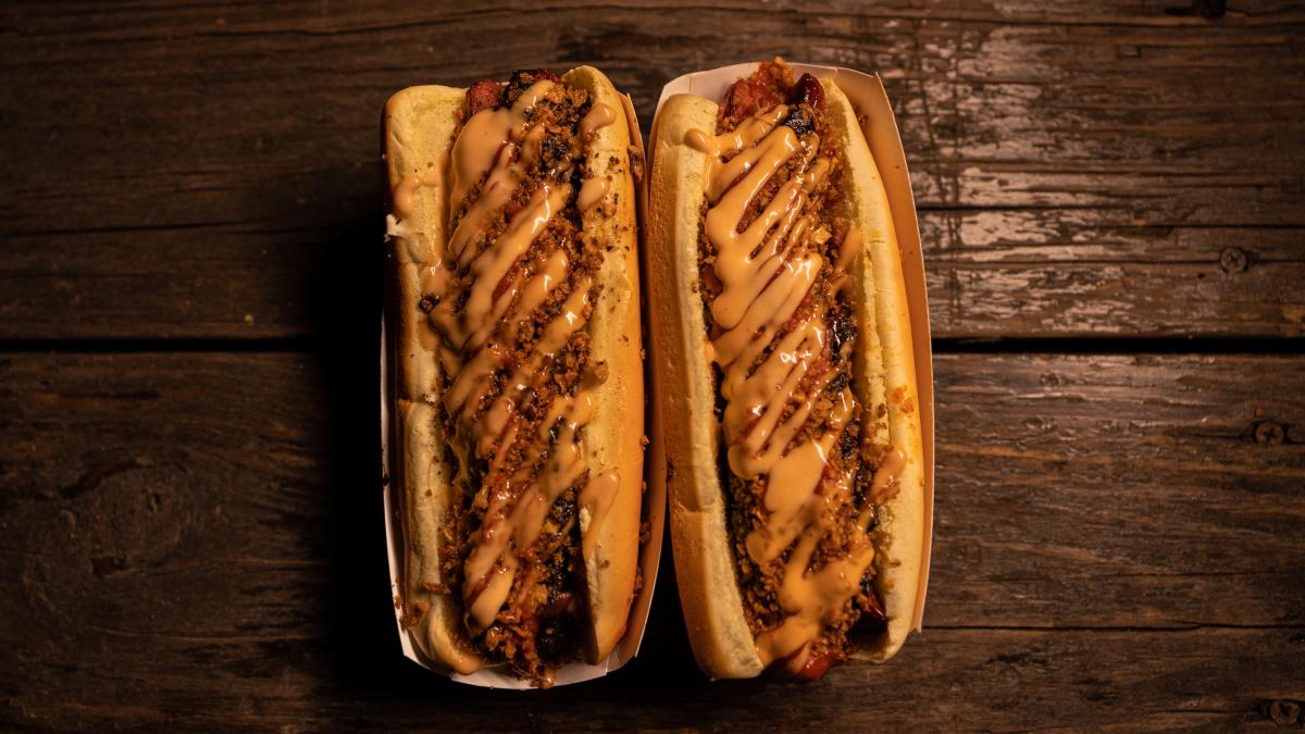 Picture taken from above of two hot dogs with chili and cheese on a brown table.